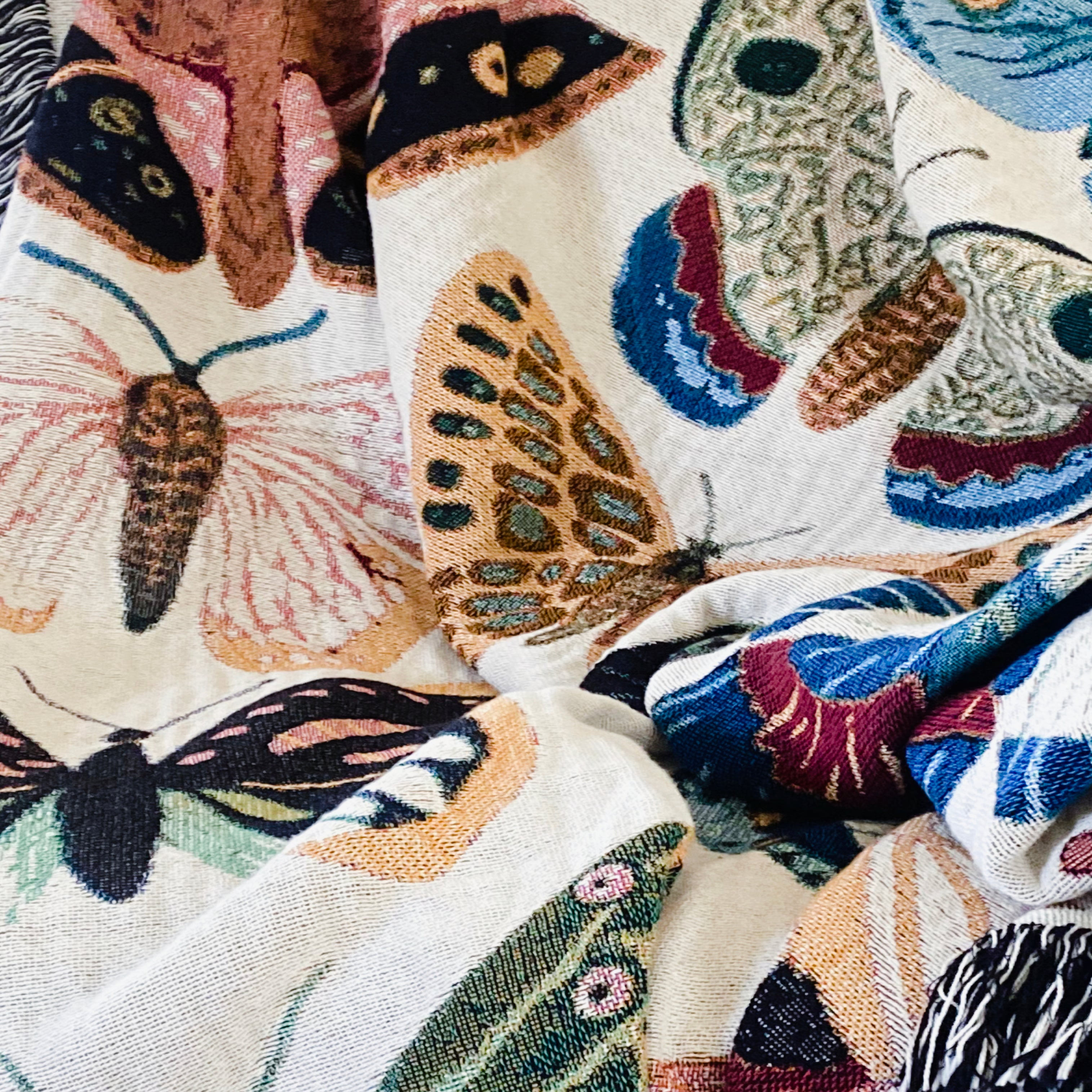 Woven throw blanket with colorful hand-drawn butterflies in pink, turquoise, yellow, coral, and green creating a joyful celebration of nature. Monarchs, swallowtails, and painted ladies flutter across soft cream fabric with decorative fringe, bringing warmth and whimsy to nurseries, dorms, and cozy spaces.