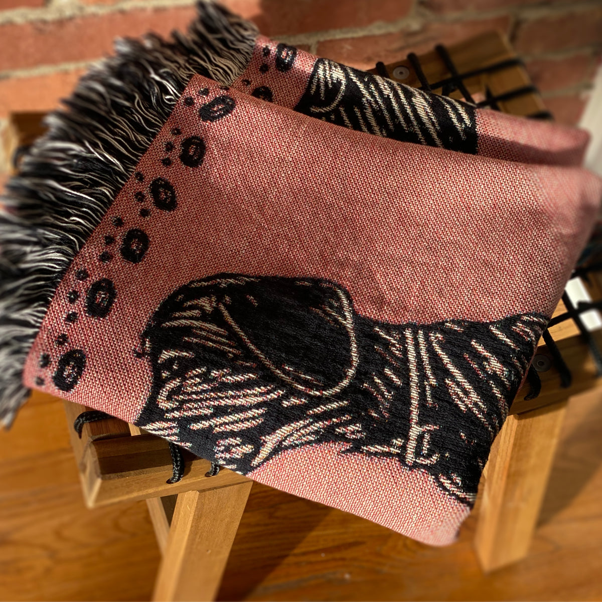 Close-up of the pink dog blanket's navy pup and paw-print border folded over a wooden chair. Playful and cozy.