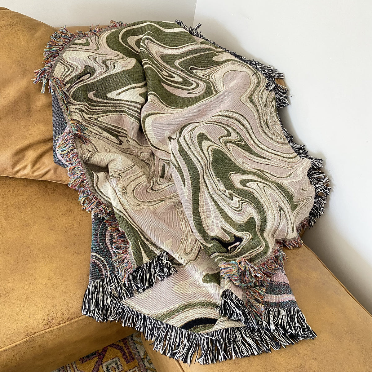 The marble blanket tossed over a tan sofa arm, its swirls and fringe in gentle folds. Relaxed and modern.
